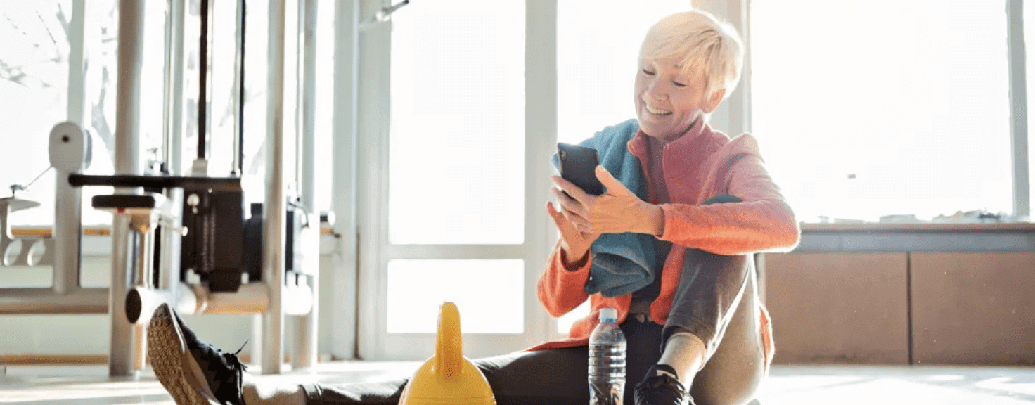 Elder woman using smartphone sitting in fitness center