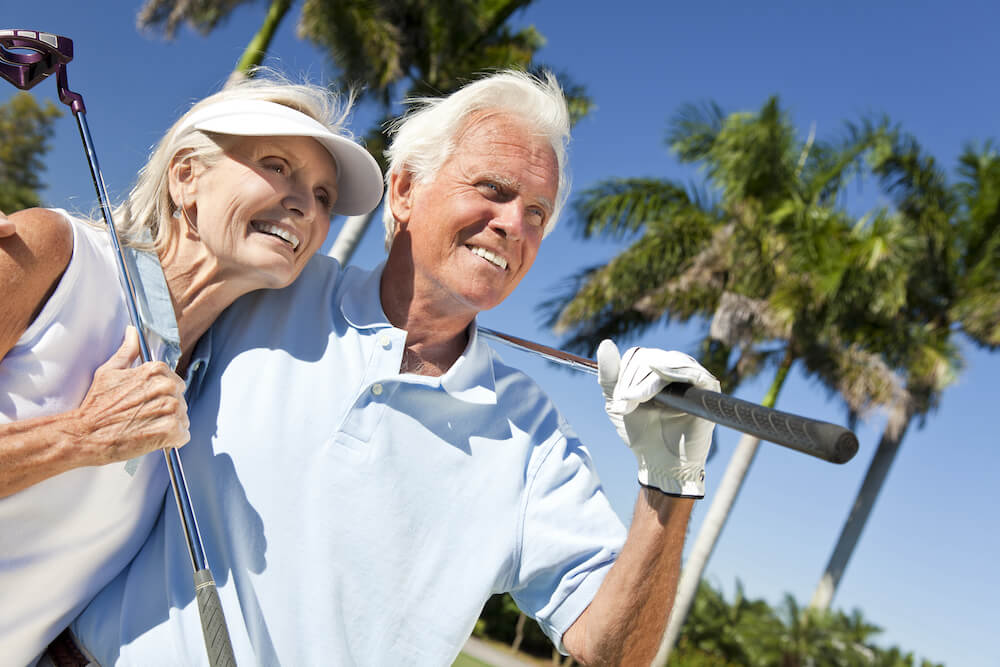 A happy senior couple who are residents at a luxury senior living community go golfing together