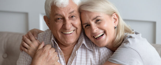 A happy senior couple hug and smile while siting on a sofa