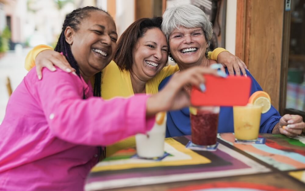 Three happy and smiling senior women take a selfie together while out to lunch