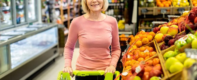 Smiling elderly woman choosing fruits at supermarket