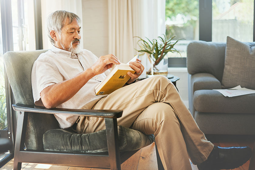 Relax, book and a senior asian man reading on a chair in the living room of his home during retirement. Study, learning and elderly person pensioner in his house alone for a literature leisure hobby.