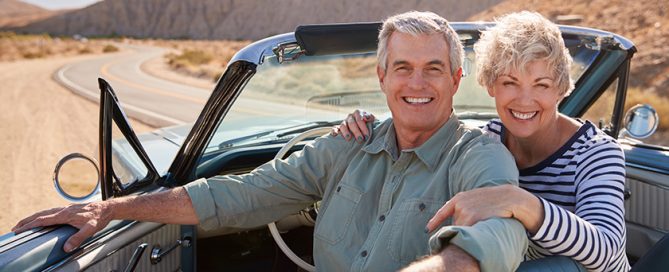 Senior couple smiling to camera from open top car