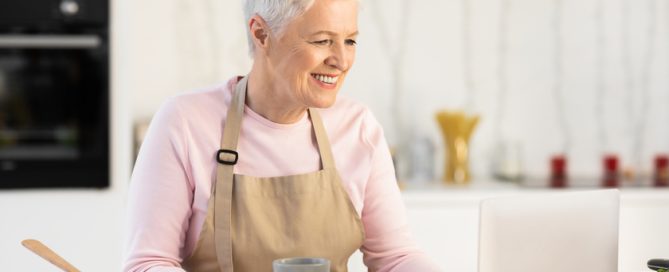 Happy Senior Woman Using Laptop Watching Cooking Video In Kitchen